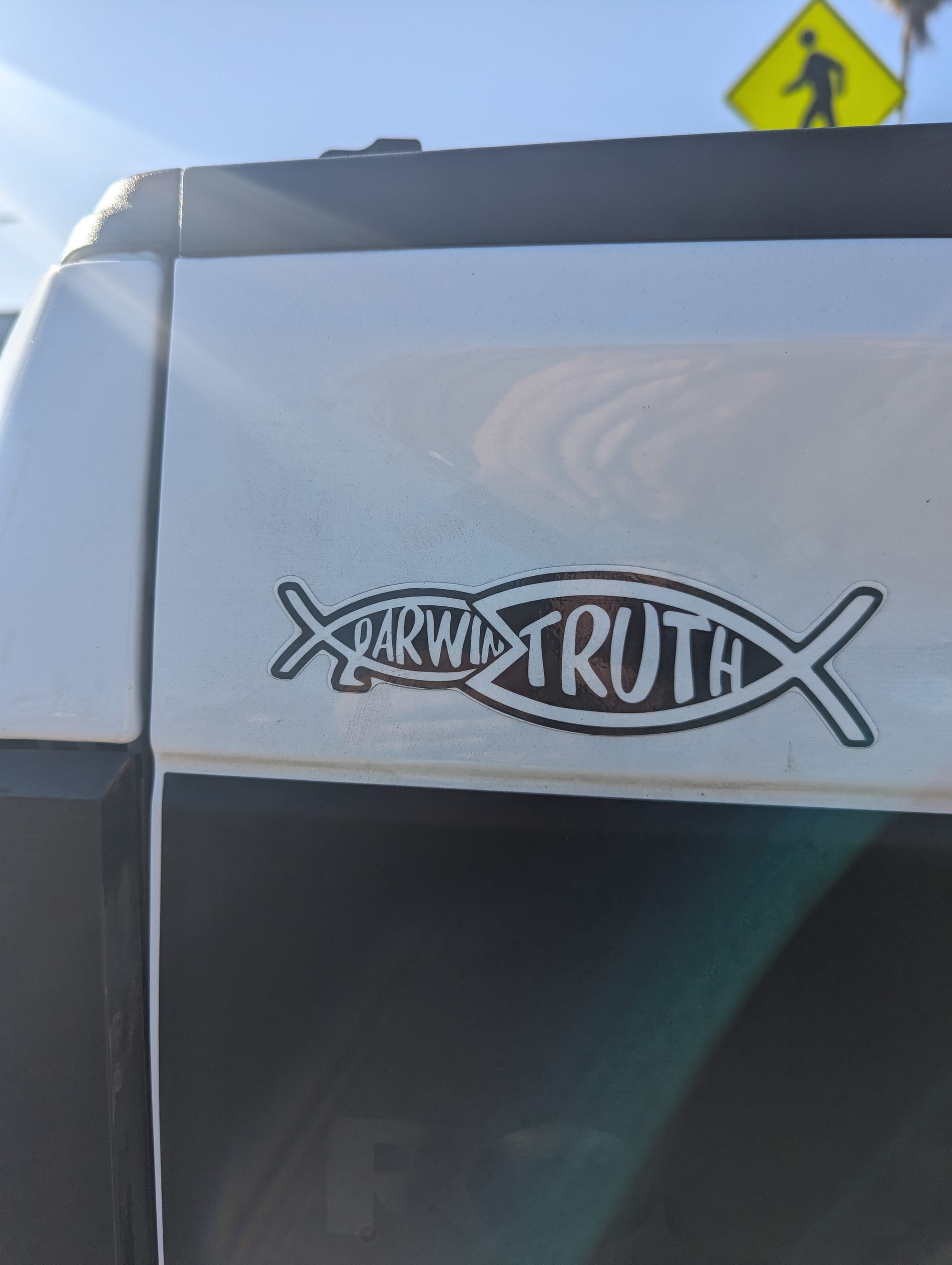 A decal on a truck shows a fish labeled "truth" eating a fish with legs labeled "Darwin"